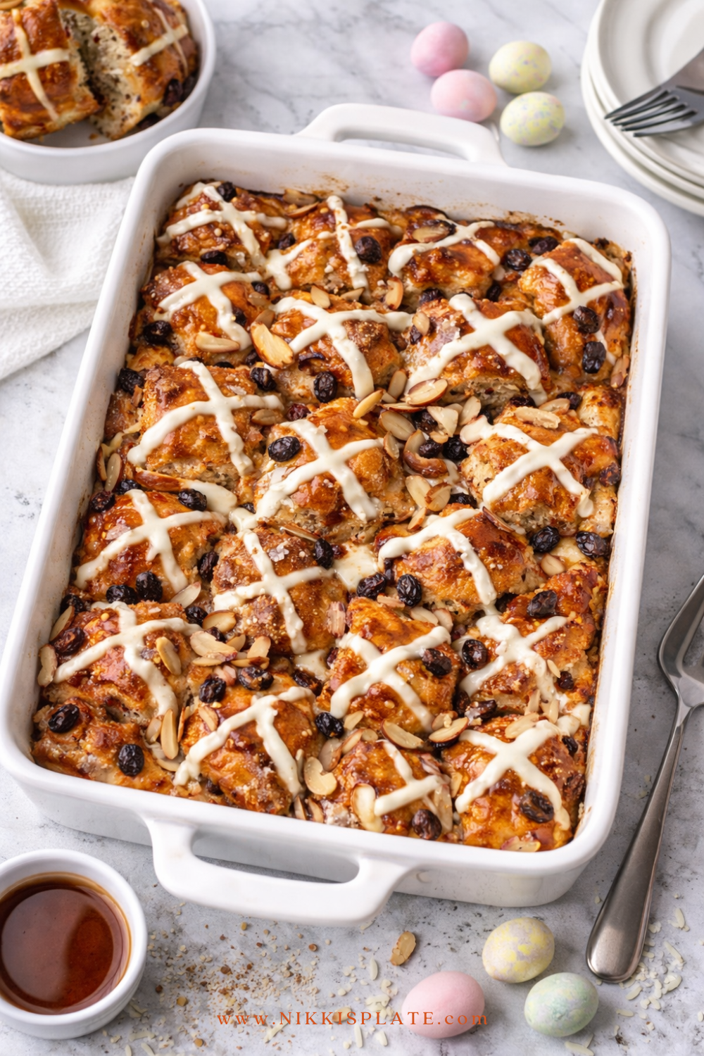 Hot Cross Bun French Toast Casserole baked in a white dish with icing drizzle, almonds, and raisins for Easter brunch