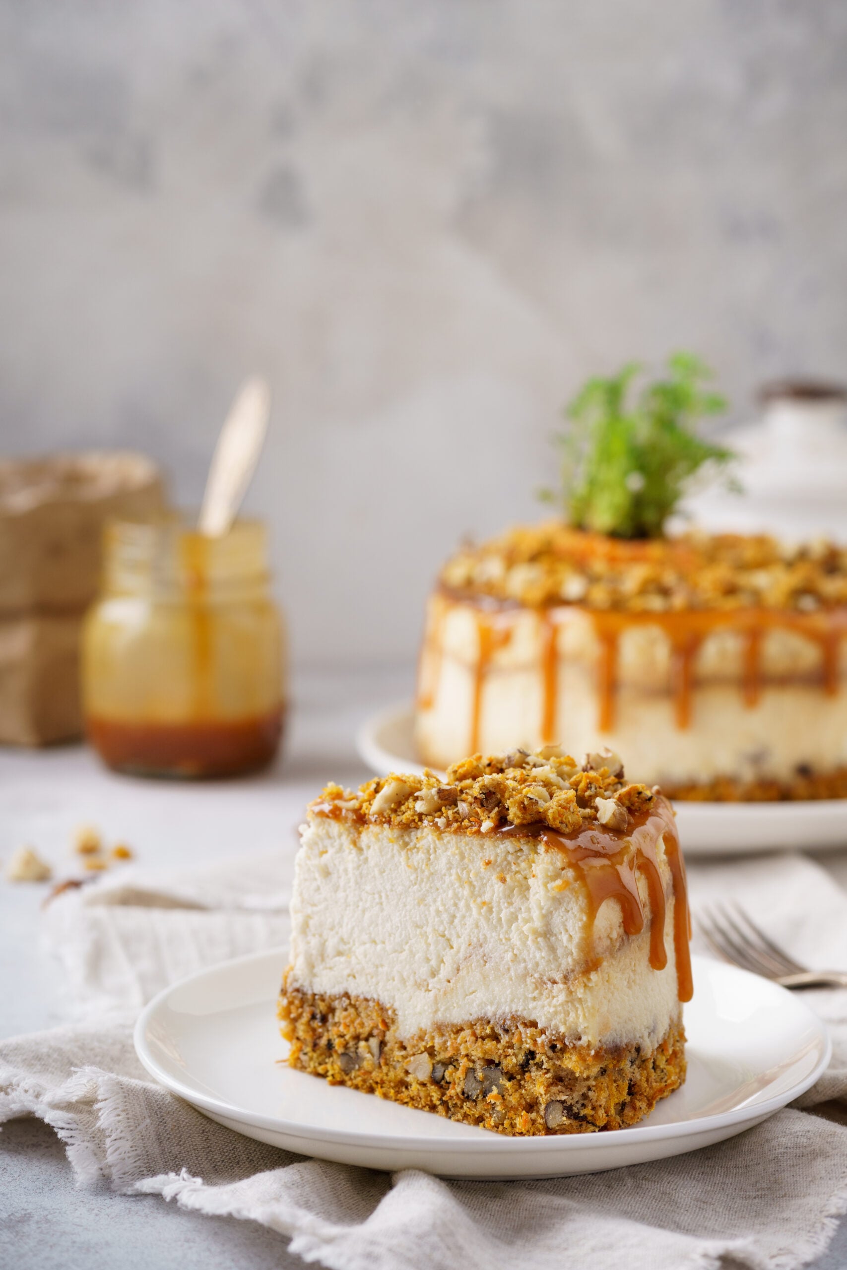 Slice of salted caramel carrot cheesecake on a white plate with caramel drizzle and whole cheesecake in background