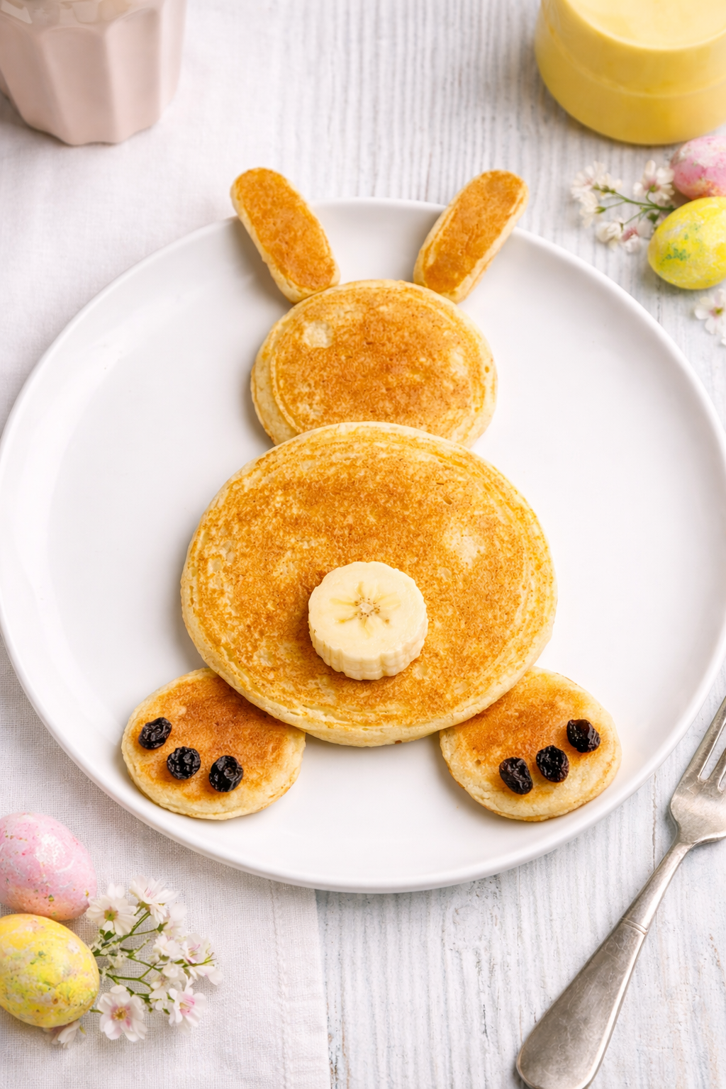 Sourdough Easter bunny pancakes shaped like a bunny on a white plate with banana slice tail and raisin details