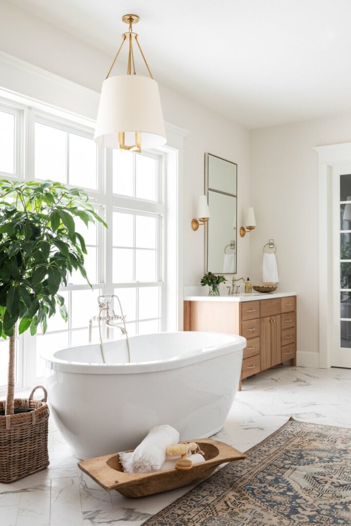 Bathrooms by Studio McGee; stand alone white bathtub, large window, greenery