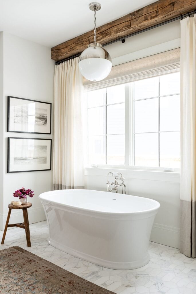 Studio McGee Bathrooms; white bathtub, wood beams, large window