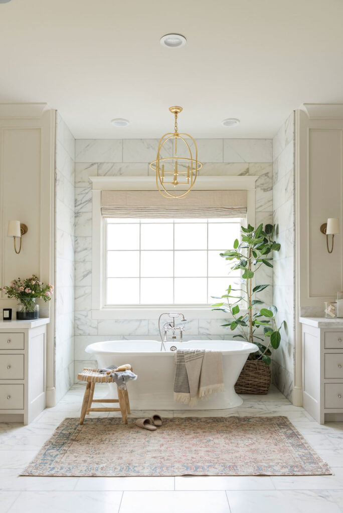 Bathrooms by Studio McGee; stand alone white tub, gold accents, greenery, large mirror