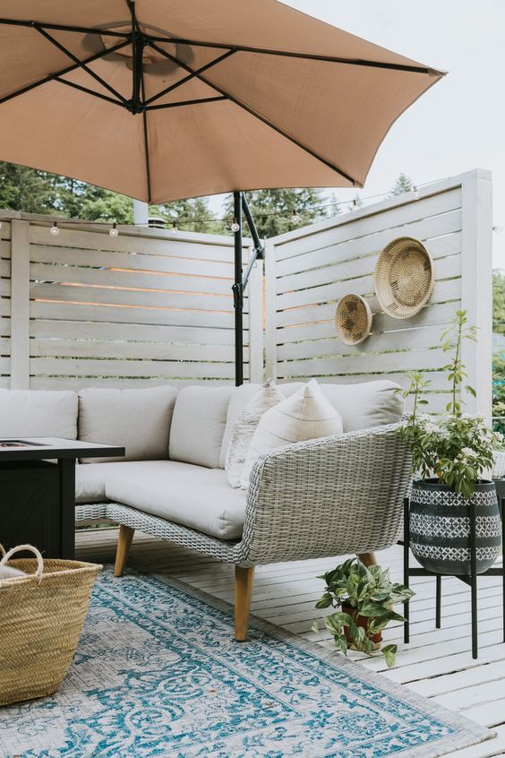Tips for Styling your Deck this Summer; umbrella, privacy wall, beige cushions, beige couch, blue rug 