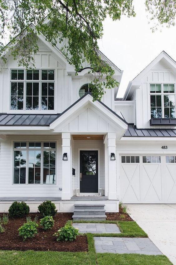 Modern Farmhouse Design Must haves: large windows, white siding, white garage door, black steel roof, white front porch