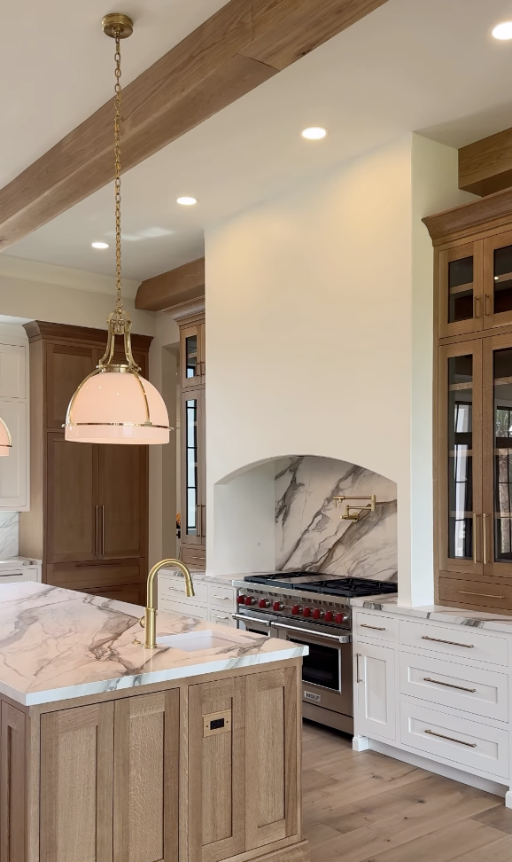 white oak kitchen with arched range hood, marble backsplash, and brass faucet