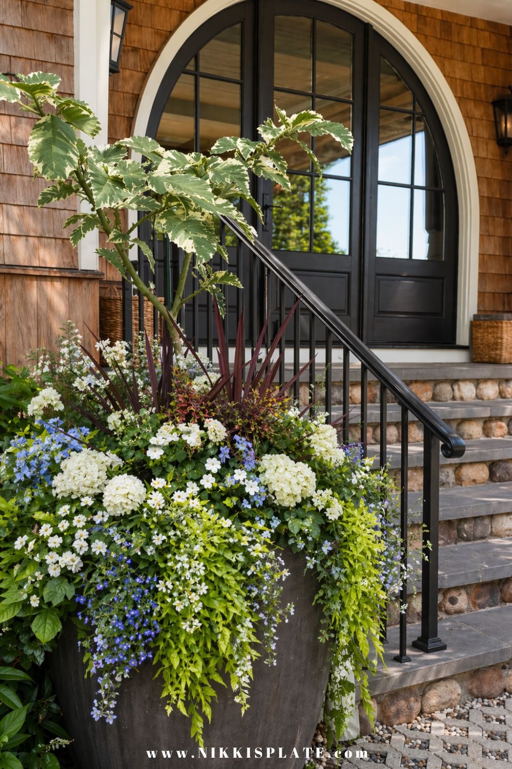 Front porch planter ideas with a large statement planter featuring layered greenery, white flowers, and trailing vines by an entryway