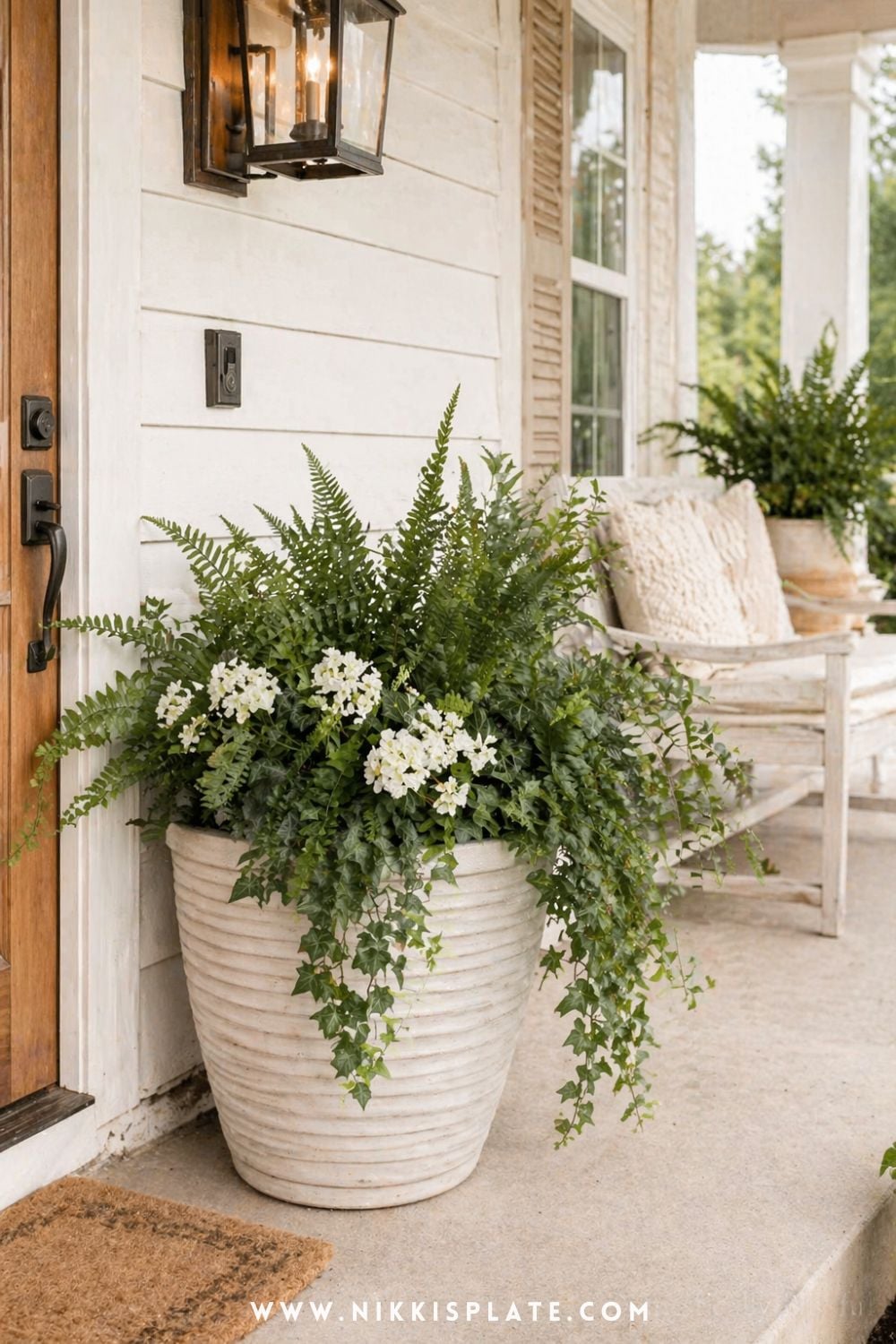 Lush front porch planter ideas with ferns, white flowers, and trailing ivy in a neutral planter by a cozy entryway