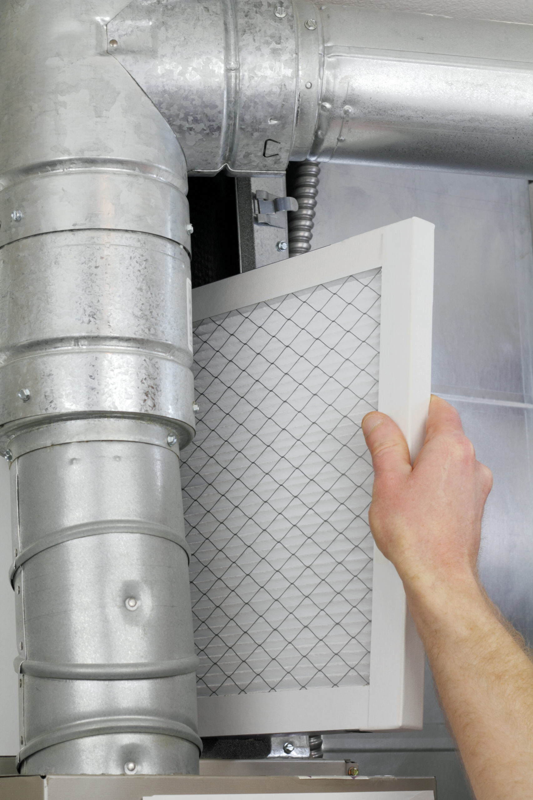 A man's arm and hand seen replacing disposable air filter in home central air furnace. - How to Make Your Home More Comfortable With the Right Air Filter