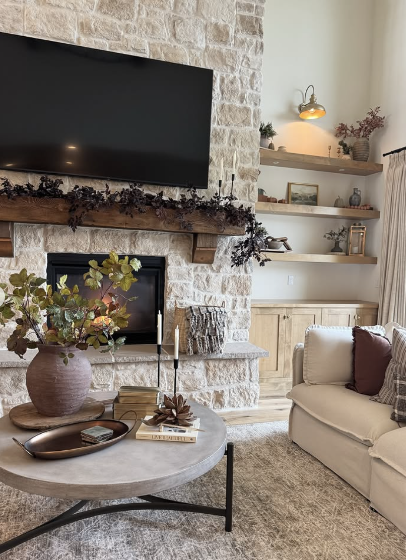 Cozy living room with stone fireplace, mounted TV above rustic wood mantel, and floating wood shelves