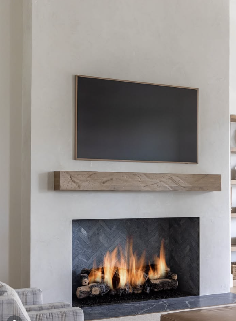 Minimalist living room with smooth plaster fireplace, mounted TV above wood mantel, and herringbone firebox interior