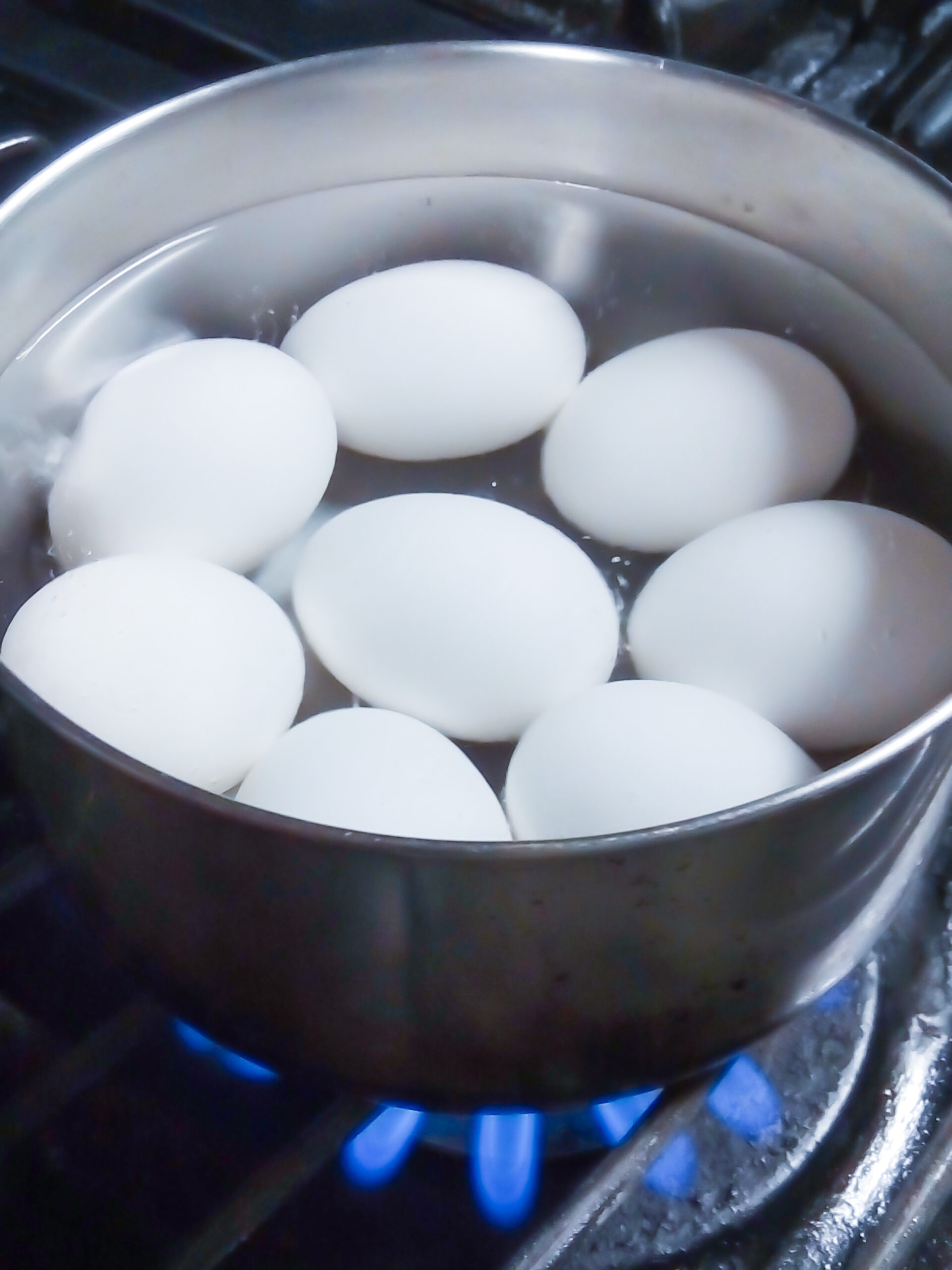 Closeup of eight hard-boiled chicken eggs cooking in pot of hot water on hot stove
