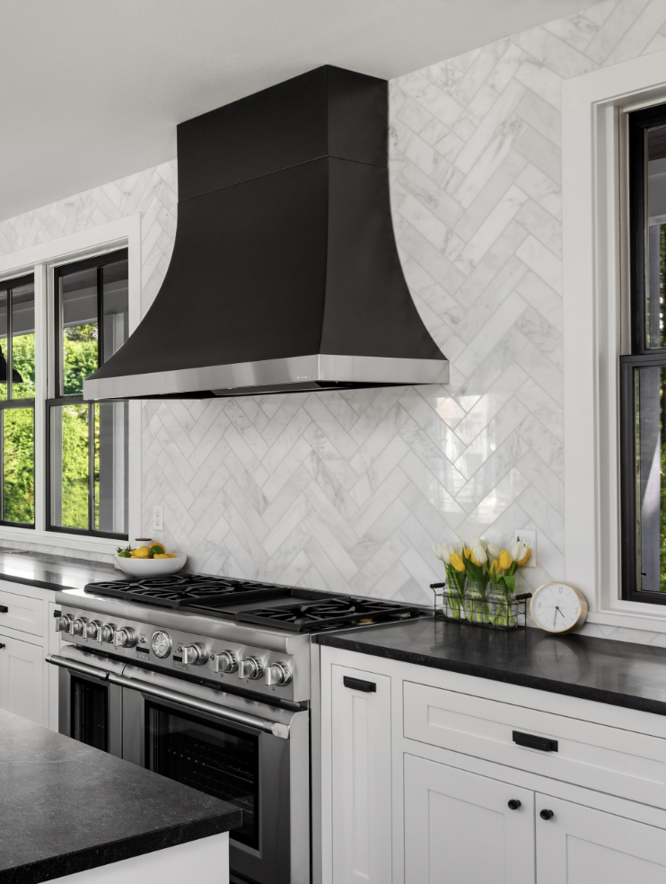 beautiful white kitchen in new luxury home with island, pendant lights, and hardwood floors. Island and Counters are Black, Hardwood Floors are Dark, and Cabinets, Backsplash, and Woodwork are White