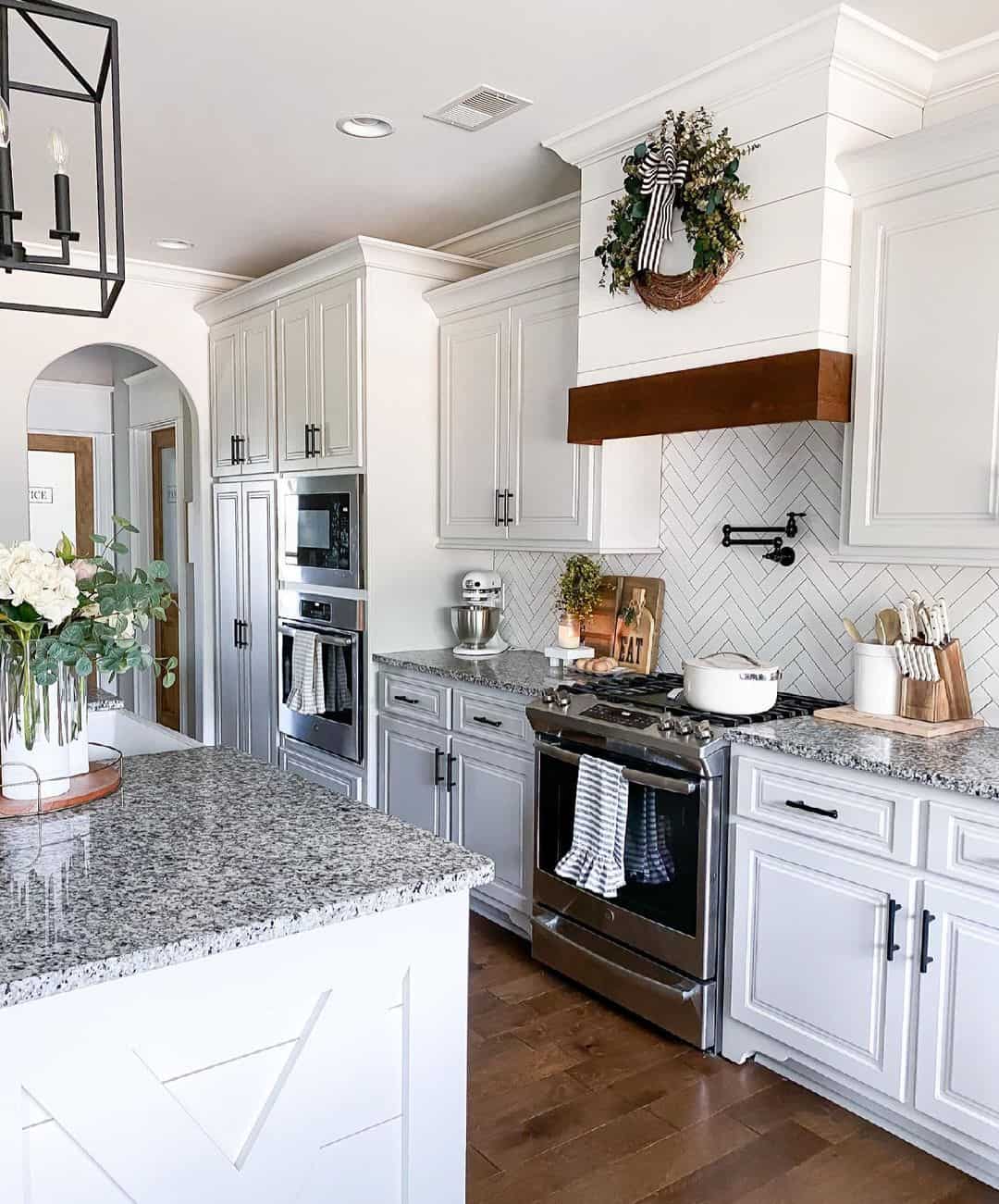 A white shiplap range hood is mounted above a stainless steel gas range. The range is fitted between white cabinets with a herringbone backsplash that has grey grout.