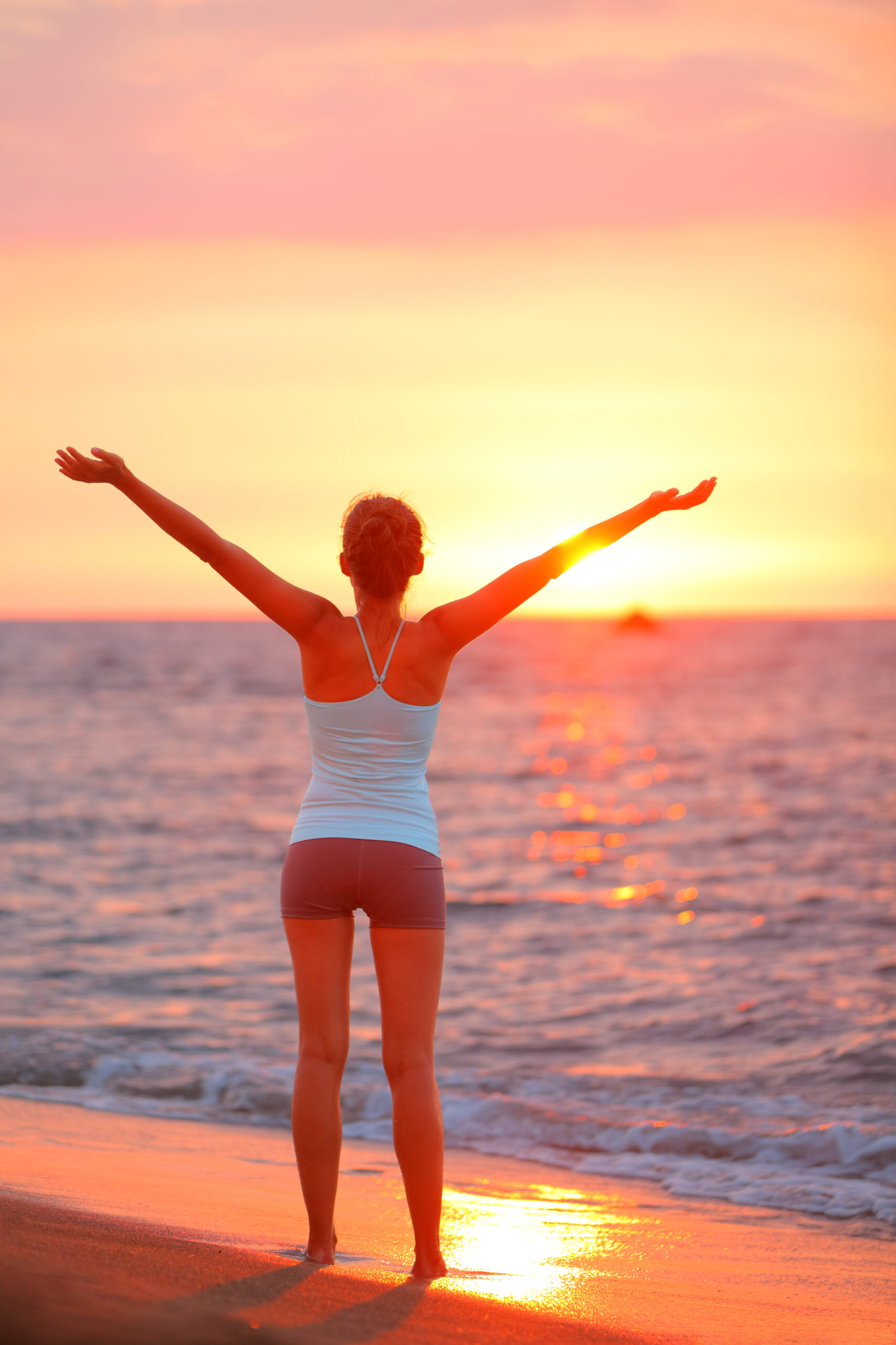 Uncovering The Joy In Everyday Wellness - Happy freedom woman relaxing arms up at beach sunset during fitness yoga. Summer vacation person carefree on holidays travel.