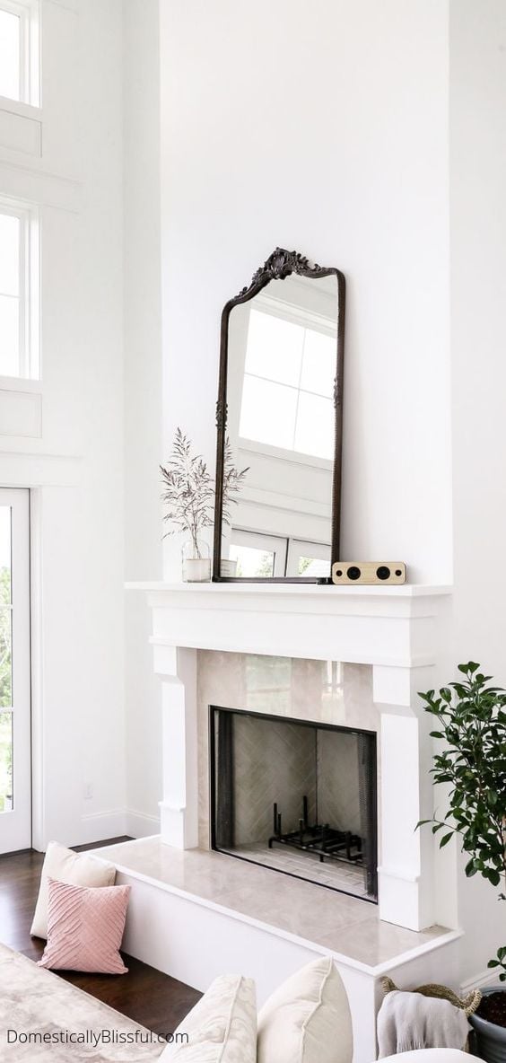 Mirror above fireplace ideas; A captivating oversized mirror takes center stage above a cozy fireplace in a living room. The size and grandeur of the mirror instantly command attention, creating a focal point that draws the eye in. Its presence not only adds a sense of depth and space to the room but also reflects and amplifies the natural light, making the entire space feel brighter and more spacious.