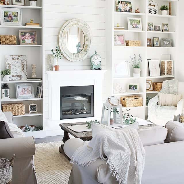 Mirror above fireplace ideas; By adding visual weight to a mantel, a thick mirror frame can create an eye-catching centerpiece on the fireplace. In this photo, an oval mirror with two wooden frames in a distressed finish has been placed on the fireplace wall. It's subdued aesthetic softly blends in with the white shiplap wall, creating a tranquil and inviting ambiance in the space. Overall, this mirror is a timeless and versatile decor element that adds both functionality and visual appeal to any room.