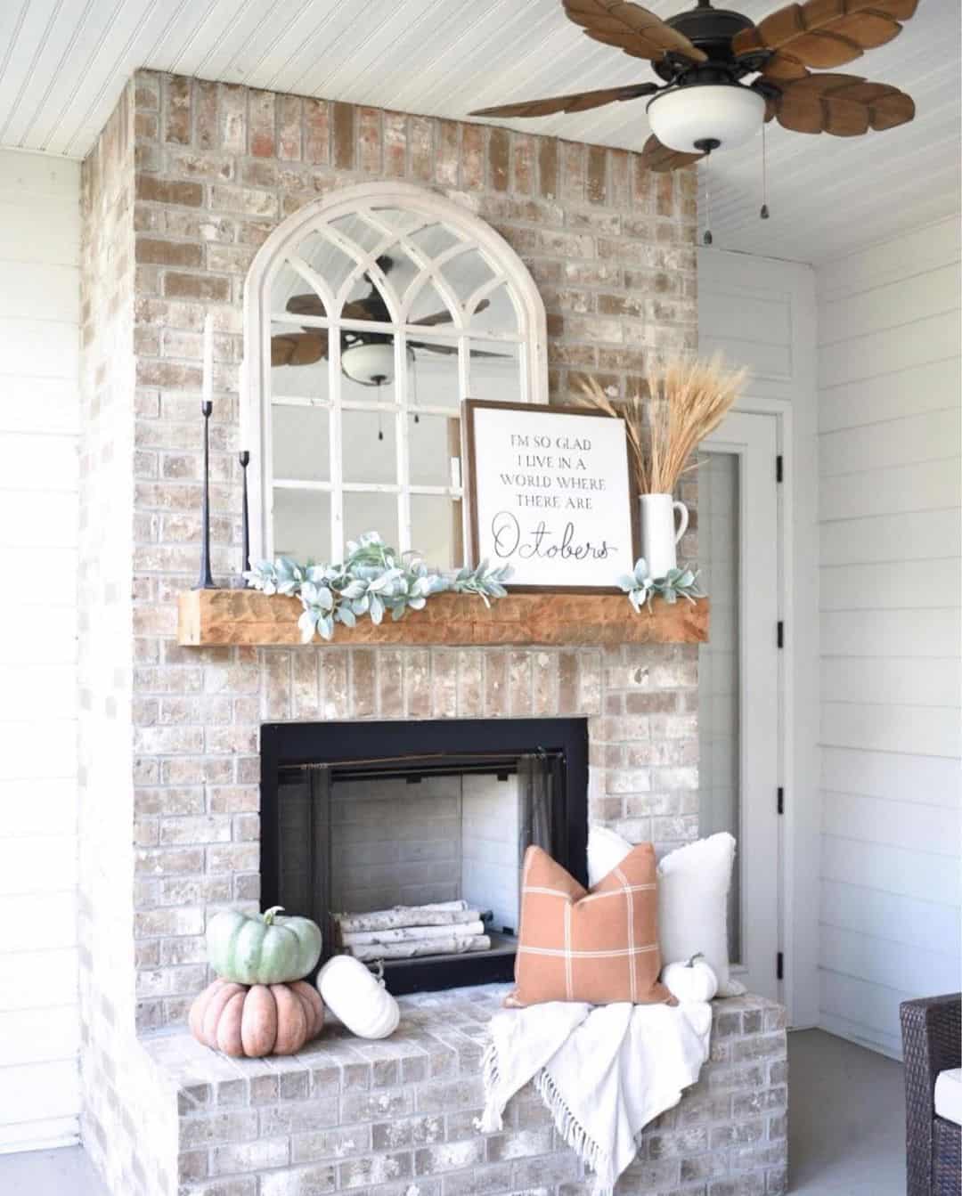 Mirror above fireplace ideas; Elevate the ambiance of a living room with a captivating arch mirror that exudes both charm and romance. The lattice design of the frame, reminiscent of a cathedral window, becomes an attention-grabbing focal point on the mantel. The distressed white paint complements the rustic brick wall flawlessly, creating a harmonious and inviting atmosphere.