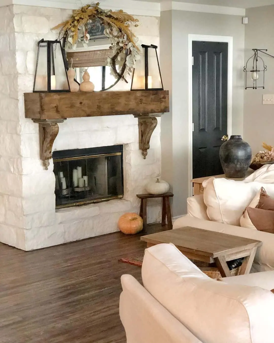 Mirror above fireplace ideas; A beautiful wreath elegantly hanging on a mirror, creating a charming focal point. The wreath's fall foliage and dull colors add a warming touch to the space. Completing the cozy ambiance, lanterns are carefully placed on the mantel, casting a warm glow and adding a hint of rustic charm.