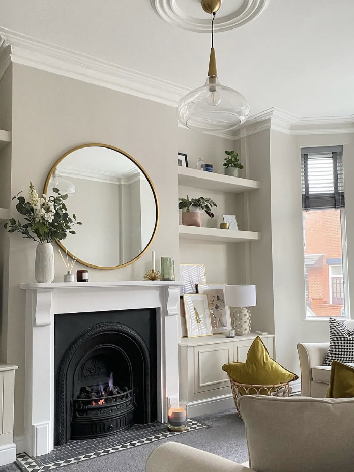 Gold round mirror above a white mantel with decorative accents, styled in a cozy neutral living room with built-in shelving and an ornate black fireplace insert.