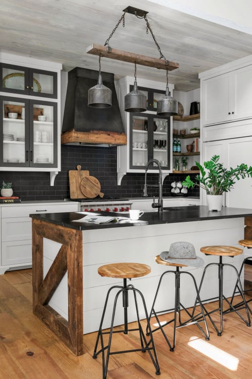 This photo showcases a charming farmhouse-style white kitchen with striking black countertops and rustic barnwood accents. The white cabinetry creates a bright and welcoming atmosphere, while the black countertops add a touch of sophistication and visual contrast. The barnwood accents, such as wooden beams or reclaimed wood shelving, add rustic charm and a sense of history to the space. The combination of elements in this design creates a harmonious balance of farmhouse warmth and modern elegance, making it an inviting and timeless kitchen space.