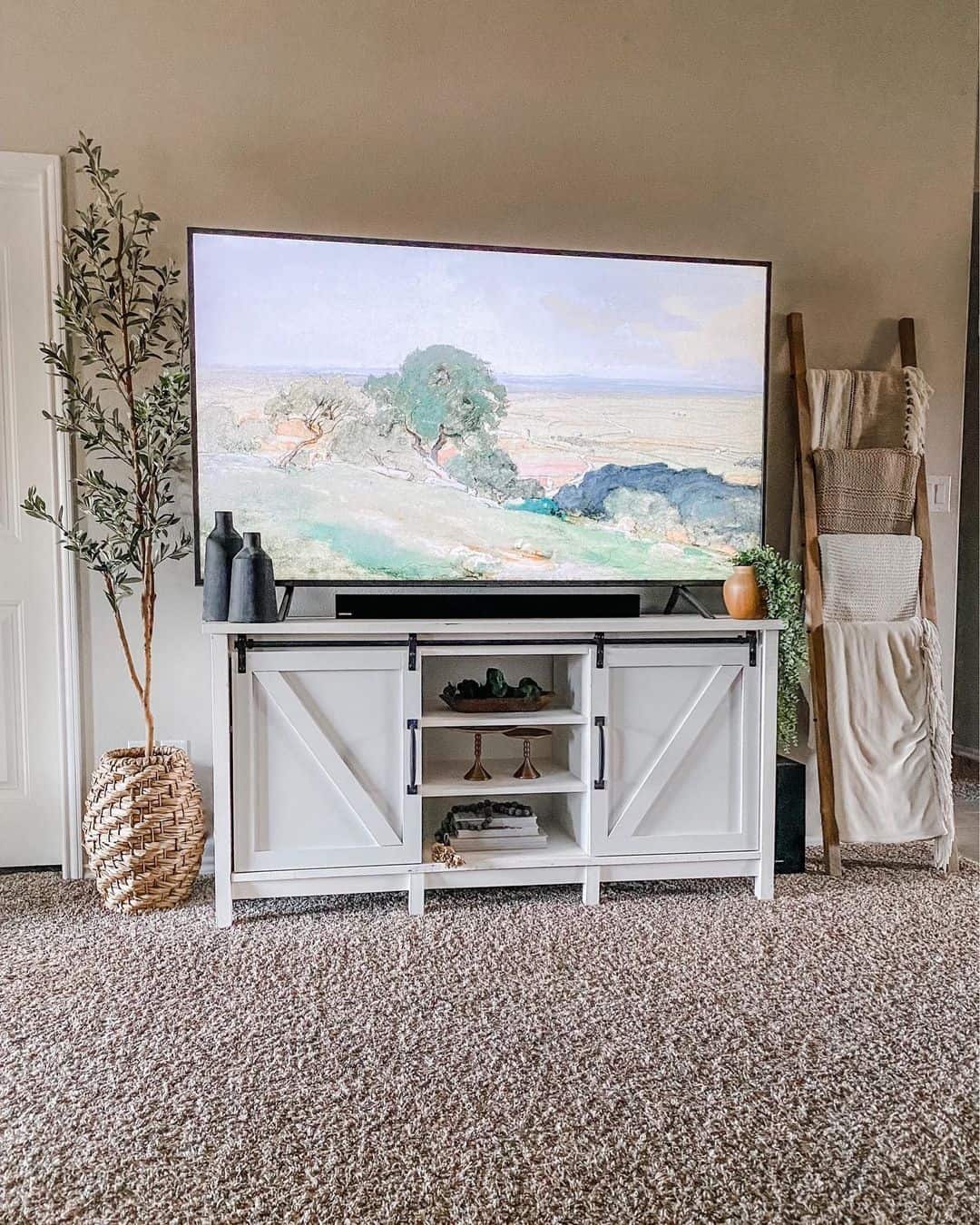 farmhouse TV stand ideas; Exuding a serene and elegant aura, this TV stand harmoniously combines white furniture with inviting warm neutral tones. The inclusion of gray vases on one side adds a touch of depth, beautifully bridging the black and white scheme of the TV console. On the other end, a captivating clay pot seamlessly connects the rich brown shades of the room to the pristine white stand, creating a cohesive and visually pleasing composition.