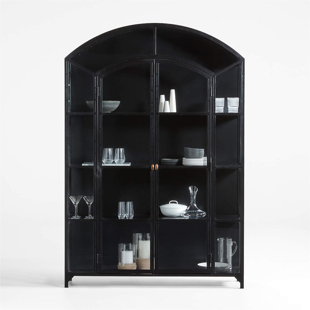 Ventana Wide Black Glass and Metal Display Storage Cabinet, is a perfect fusion of Old World charm and contemporary design. Its zinc-colored iron construction features a captivating arch that beautifully contrasts with the black-painted engineered wood shelves. The light-reflecting glass panes enhance the visual appeal of your display, making this cabinet ideal for your library or living room. Meticulously handcrafted, welding marks are visible as a testament to the fine workmanship of the piece.