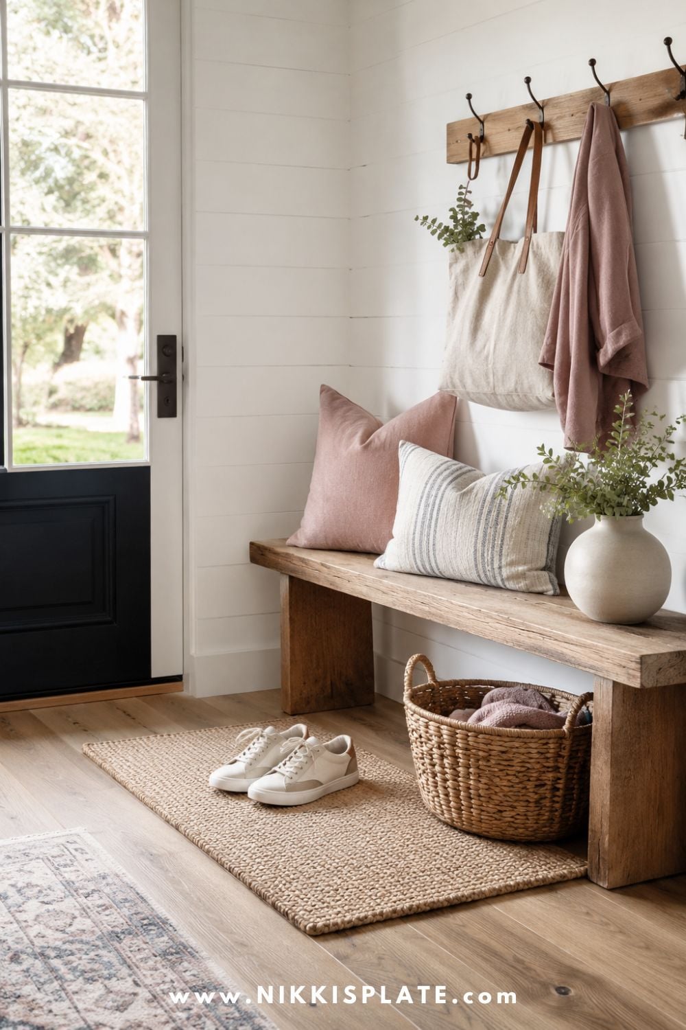Bright modern farmhouse entryway with neutral shoes left on a woven mat beside a rustic wood bench, wicker basket, linen tote, blush accents, and fresh greenery.