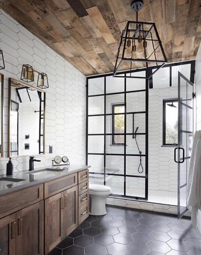 Black hexagon tile bathroom floor paired with white hexagon wall tile, a black-framed glass shower, and warm wood vanity.