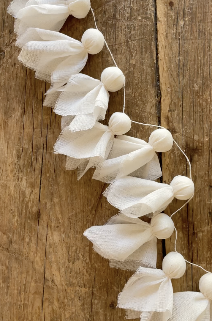 Handmade ghost garland made with small fabric-wrapped ghost shapes tied onto a string, displayed on a rustic wooden background. DIY Ghost Decoration Ideas