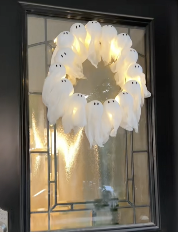 DIY ghost wreath made from small glowing ghosts arranged in a circle, hanging on a glass front door for Halloween.