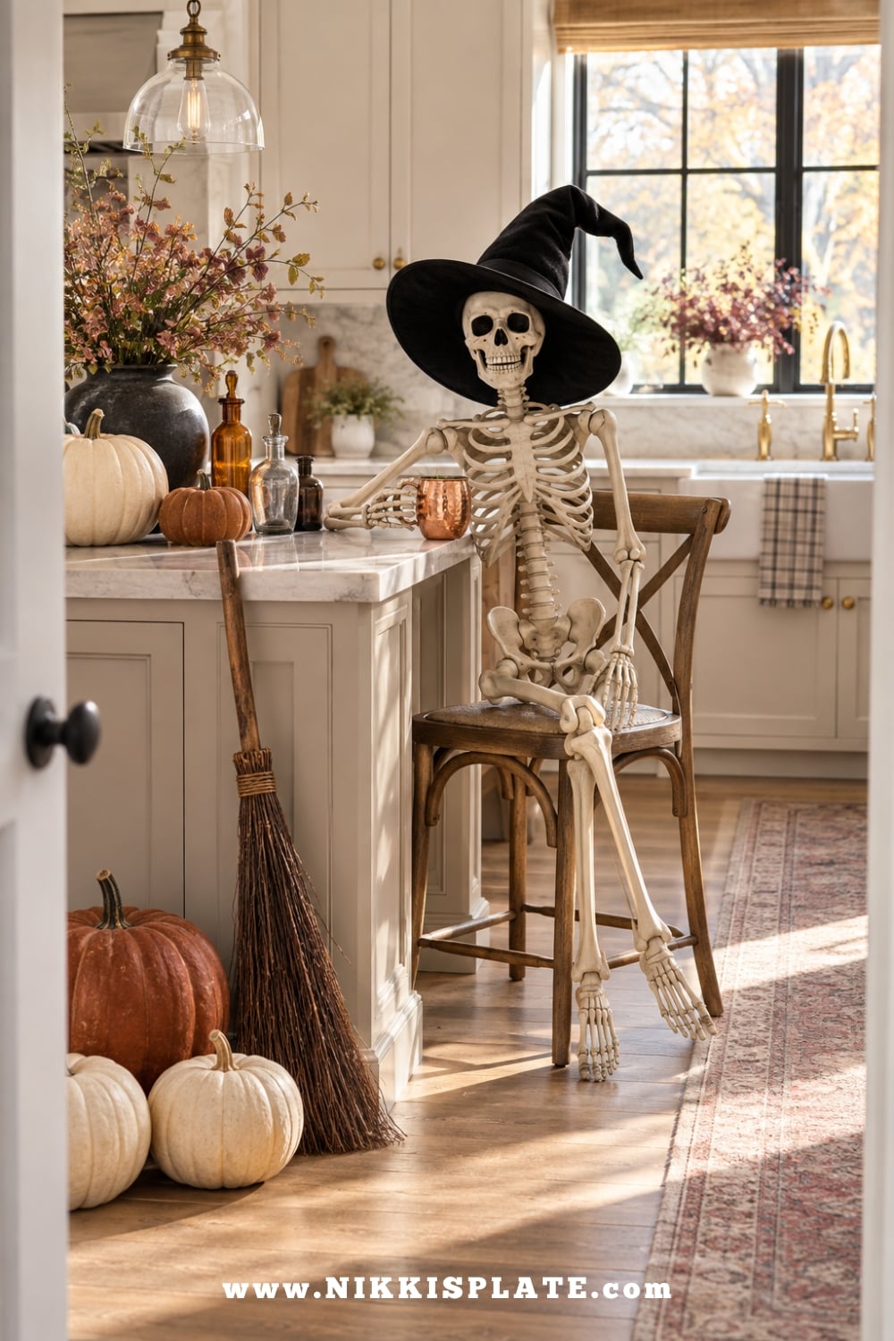 Skeleton wearing a black witch hat seated beside a cozy farmhouse kitchen display
