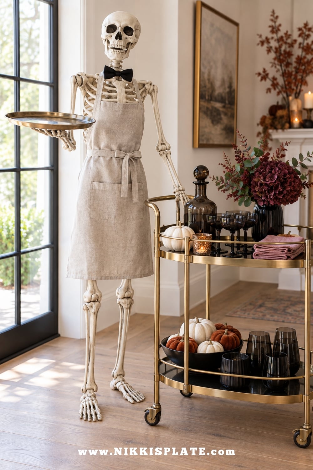 Skeleton dressed as a butler holding a tray beside a styled brass Halloween bar cart