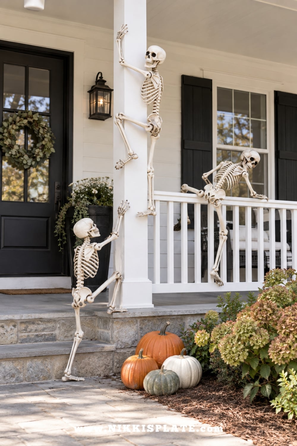 Three poseable skeletons arranged as if climbing a low white farmhouse porch column