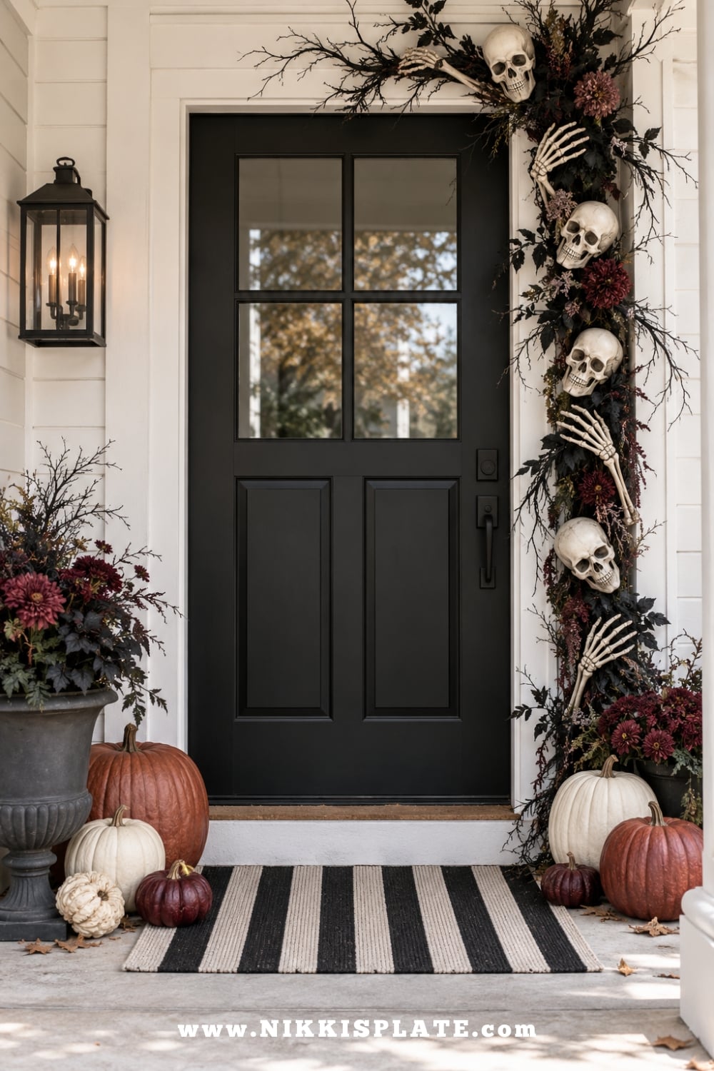 Black front door styled with lightweight skulls, skeleton hands, dark branches and burgundy pumpkins