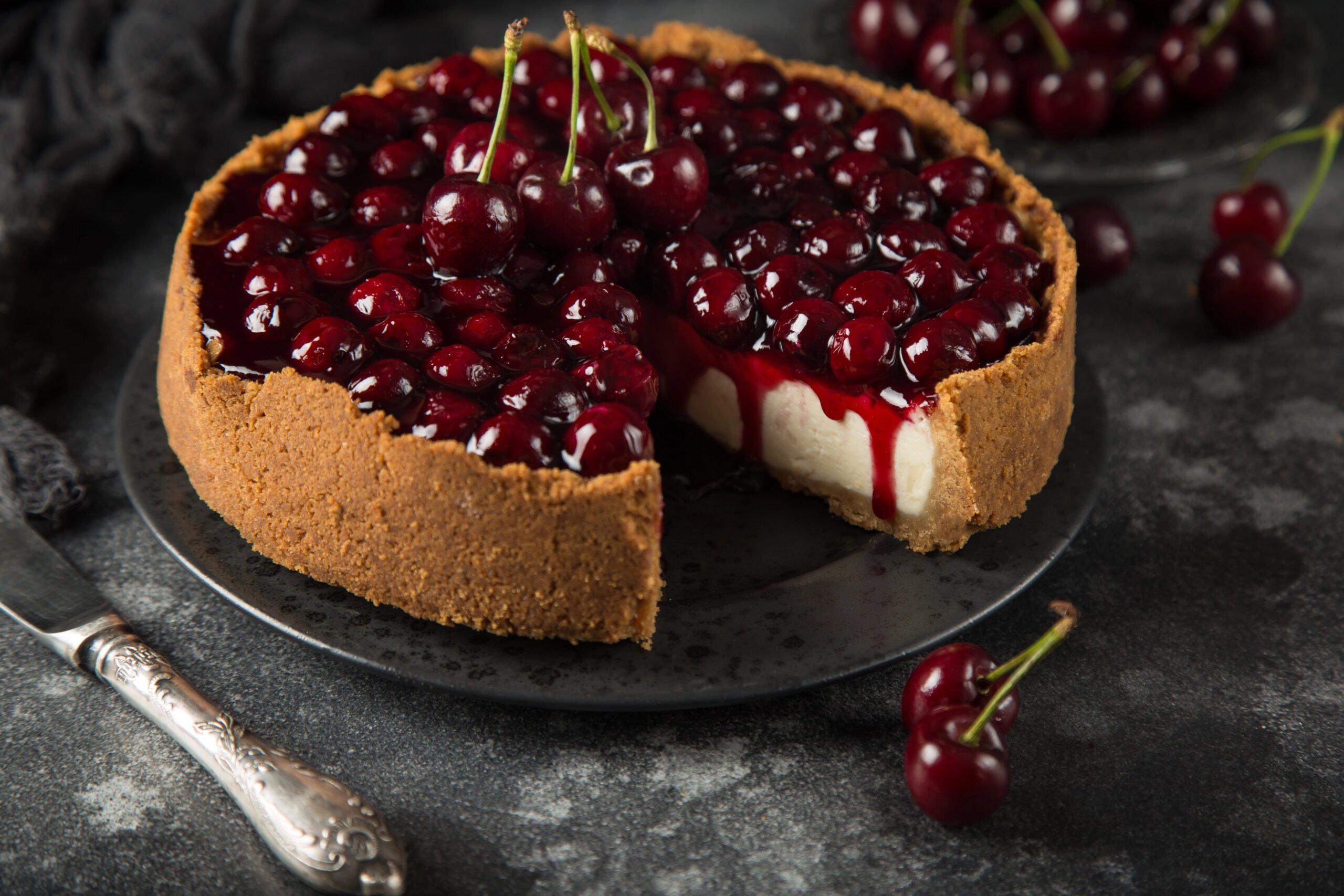 Cherry cheesecake with a slice removed, showing creamy filling and cherry topping dripping onto the graham cracker crust.
