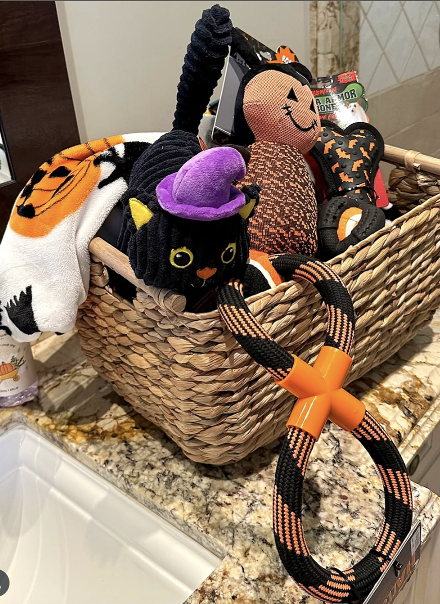 Woven Halloween-themed boo basket for dogs filled with festive plush toys, a rope tug toy, pumpkin blanket, and spooky chew bones on a kitchen counter
