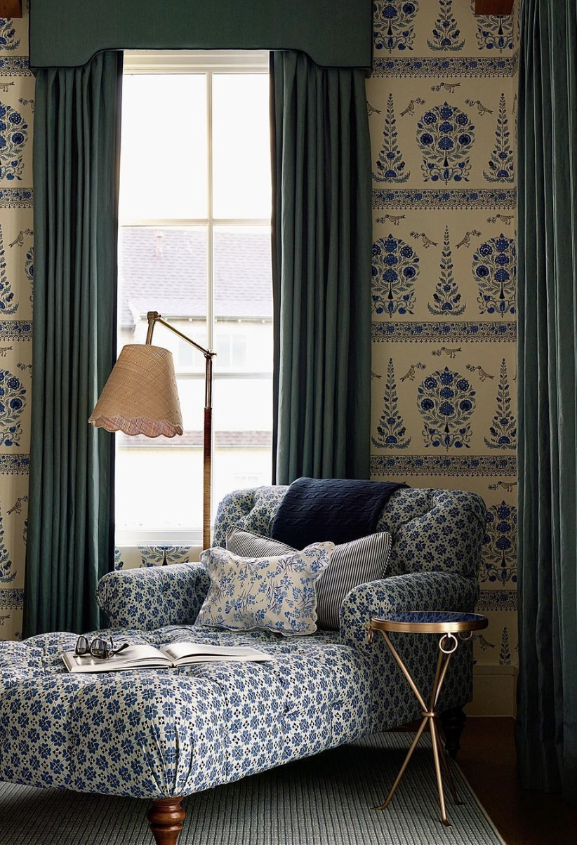 Floral blue and white chaise lounge reading nook with traditional wallpaper, velvet curtains, and a brass side table