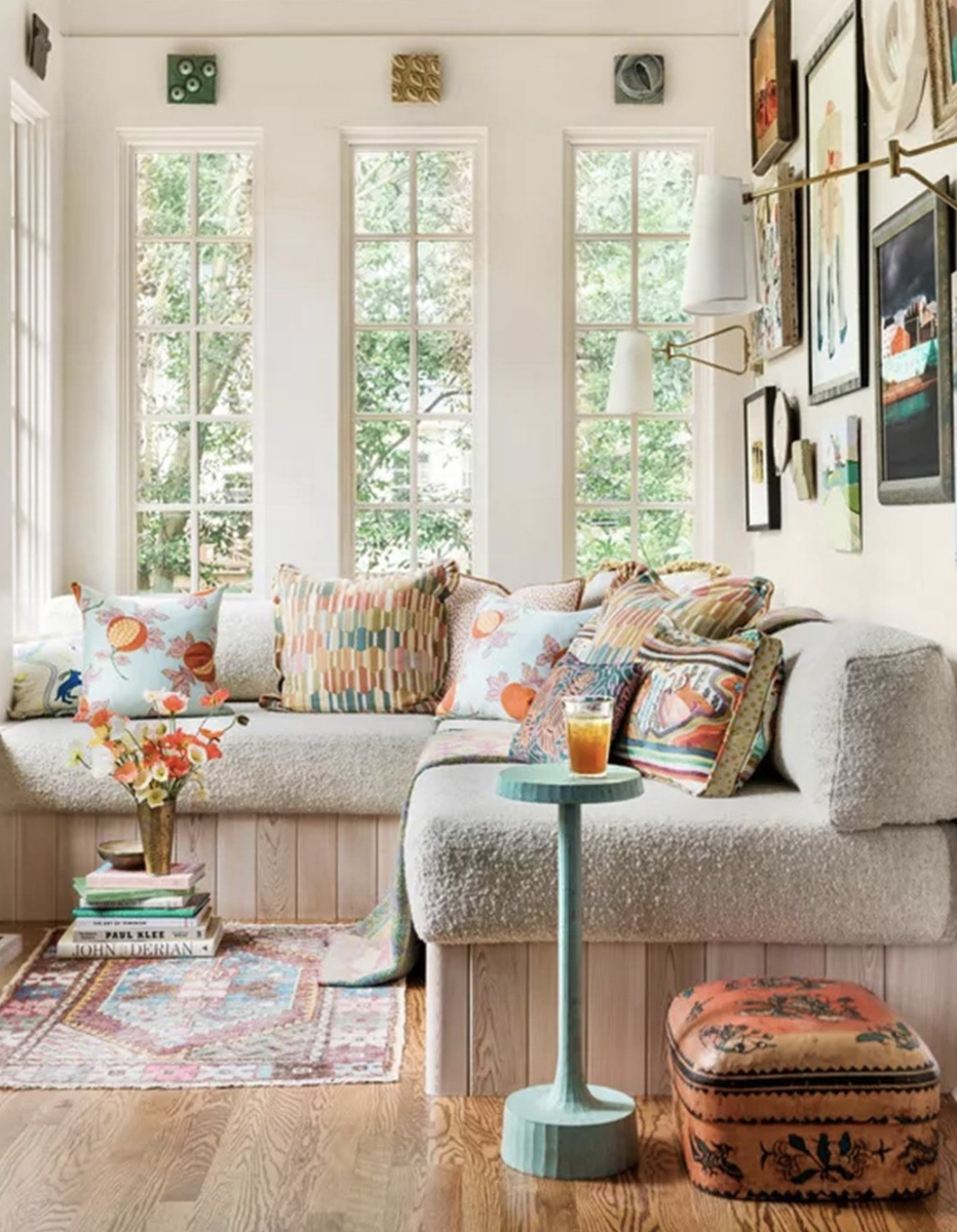Bright reading nook with a cream sectional, colorful pillows, vibrant gallery wall, and tall windows letting in natural light