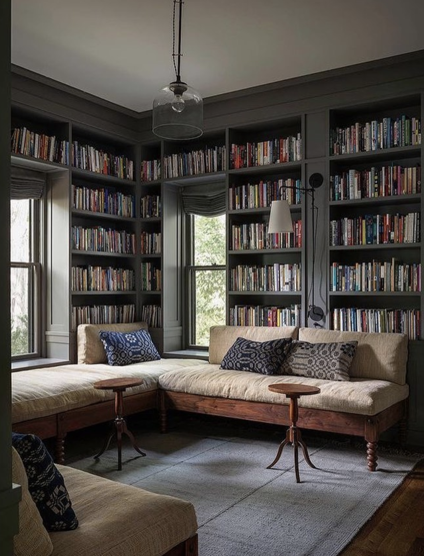 Corner library reading nook with dark built-in bookshelves and cushioned daybeds