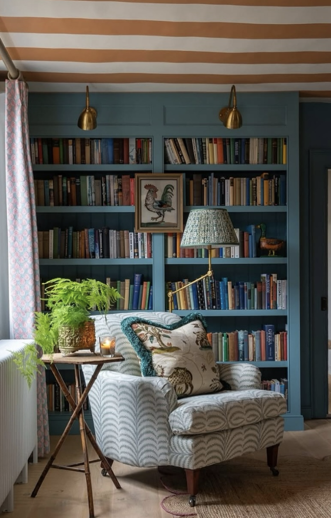 Cozy reading nook with blue built-in bookshelves, patterned armchair, and striped ceiling