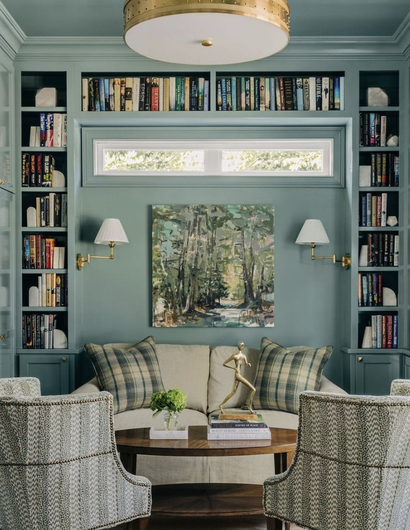 Blue reading nook with built-in bookshelves, plaid pillows, round coffee table, and gold accents
