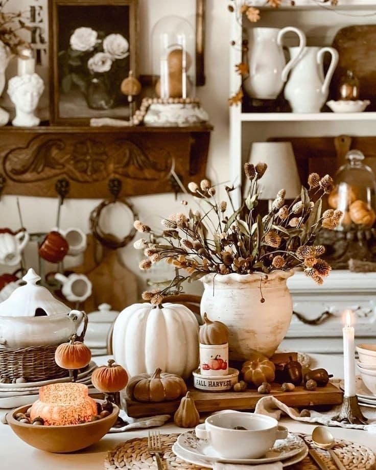 Farmhouse fall tablescape featuring dried florals, white pumpkins, acorns, candles, and vintage-style pottery.