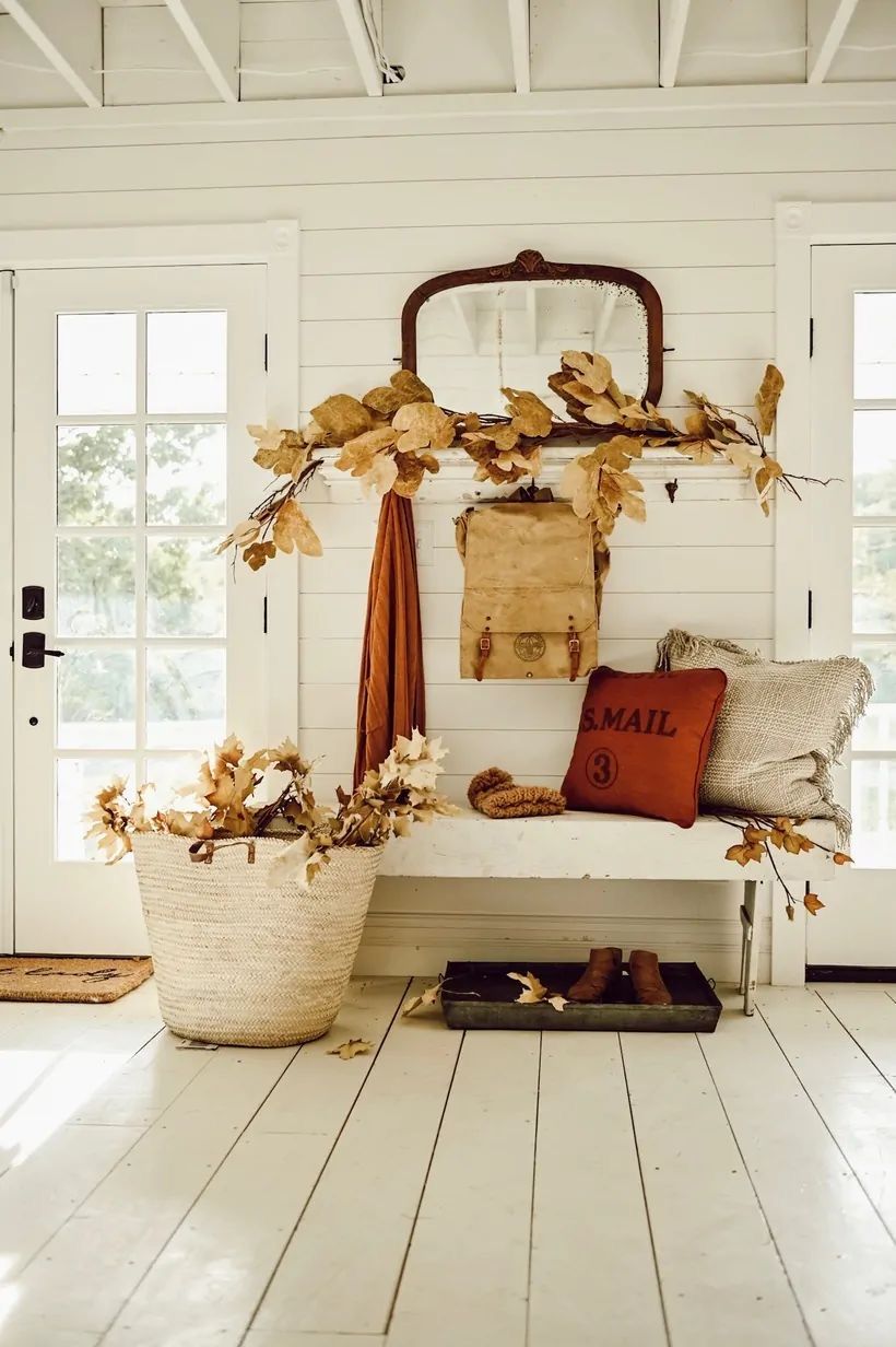 Farmhouse fall entryway with bench, leaf garland, vintage mirror, pillows, and woven basket of autumn branches