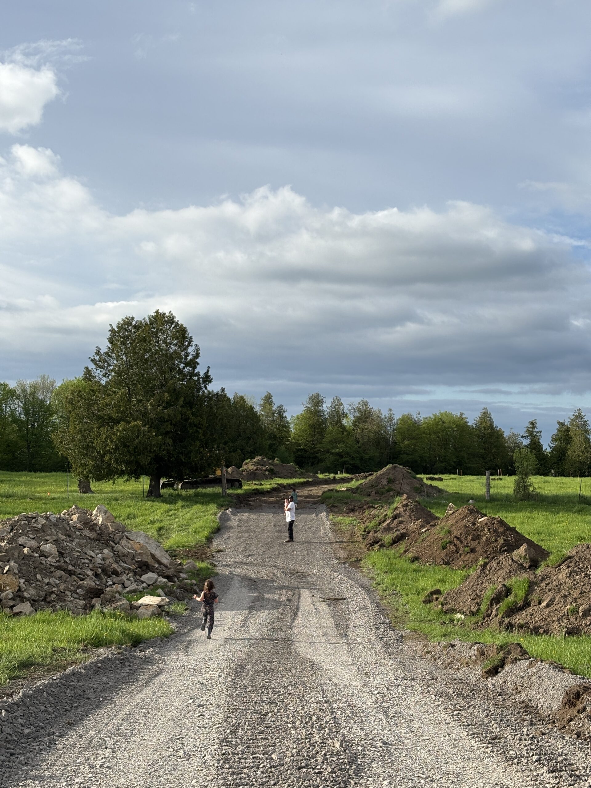 Children and adults exploring the new rural driveway surrounded by dirt piles and cleared land.