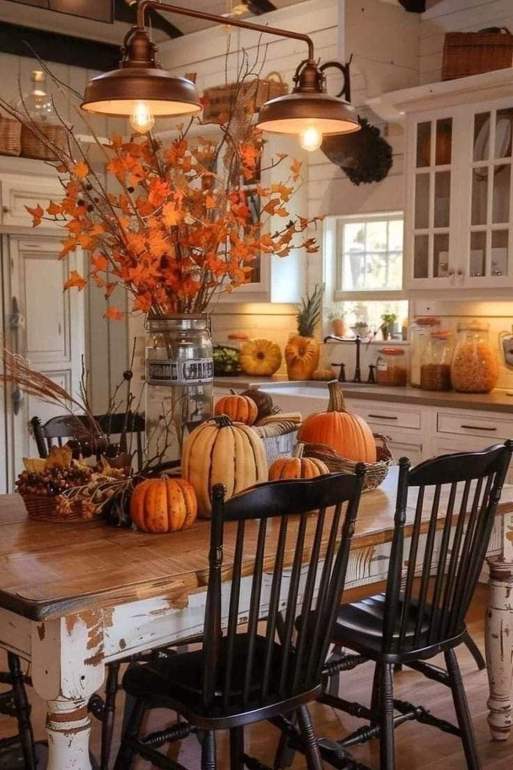 Rustic farmhouse kitchen with pumpkins, fall foliage, and vintage decor on a distressed wood table under warm lighting.