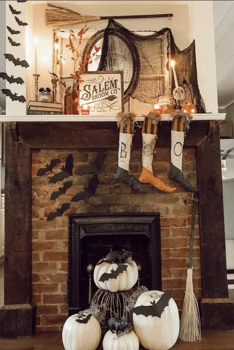 Farmhouse fireplace with white pumpkins, paper bats, Salem Broom Co. sign, candles, witch stockings, and gauzy black draping