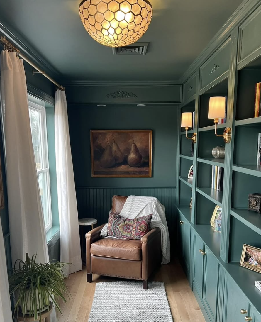Reading nook with dark green built-in shelves, leather armchair, and vintage artwork