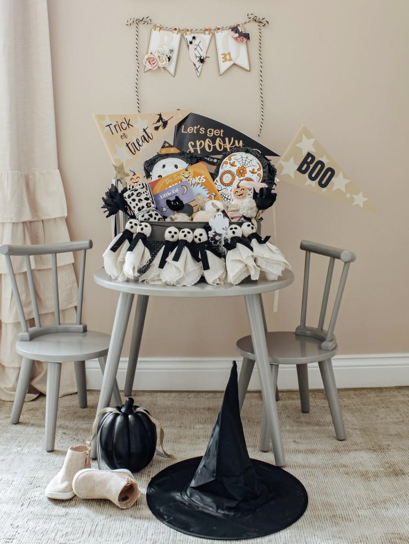 Neutral-themed boo basket for kids on a playroom table, filled with books, ghost decorations, Halloween signs, and soft accessories.