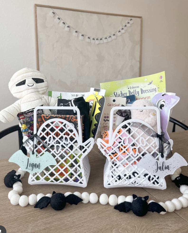 Personalized ghost-shaped boo baskets for kids filled with Halloween books, treats, and toys, labeled with names Logan and Julia.