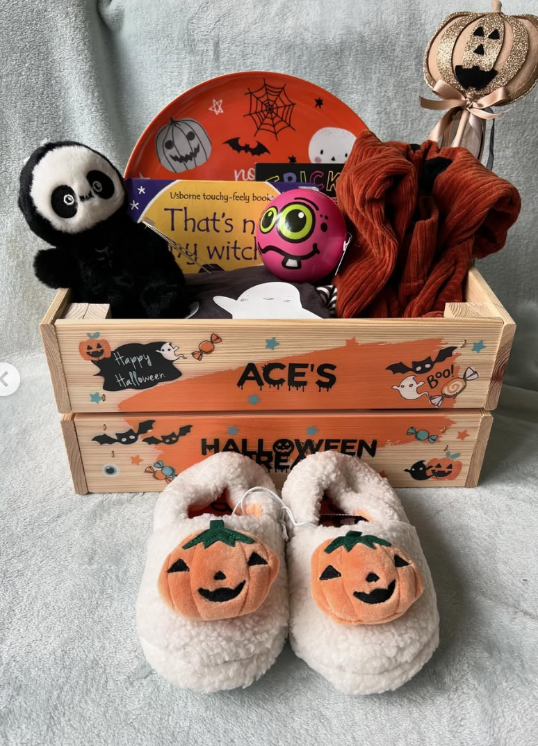 Personalized Halloween boo basket for toddlers with plush pumpkin slippers, books, a panda plush toy, and festive clothes in a wooden crate labeled “Ace’s Halloween Treats.”